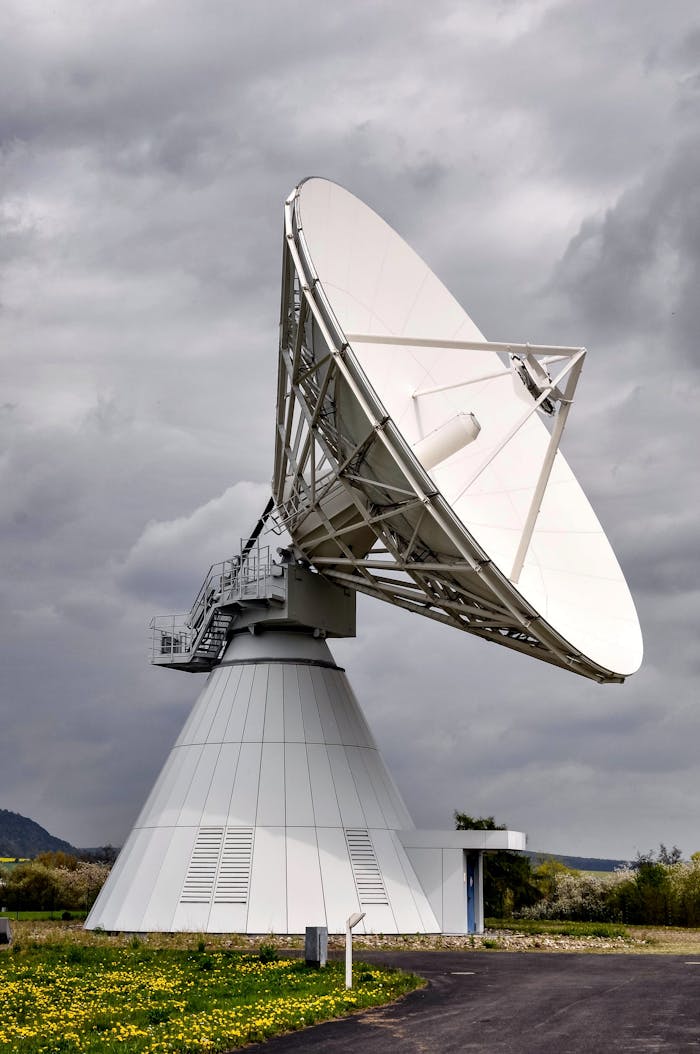 A large satellite dish in a rural area under a cloudy sky, showcasing telecommunication technology.